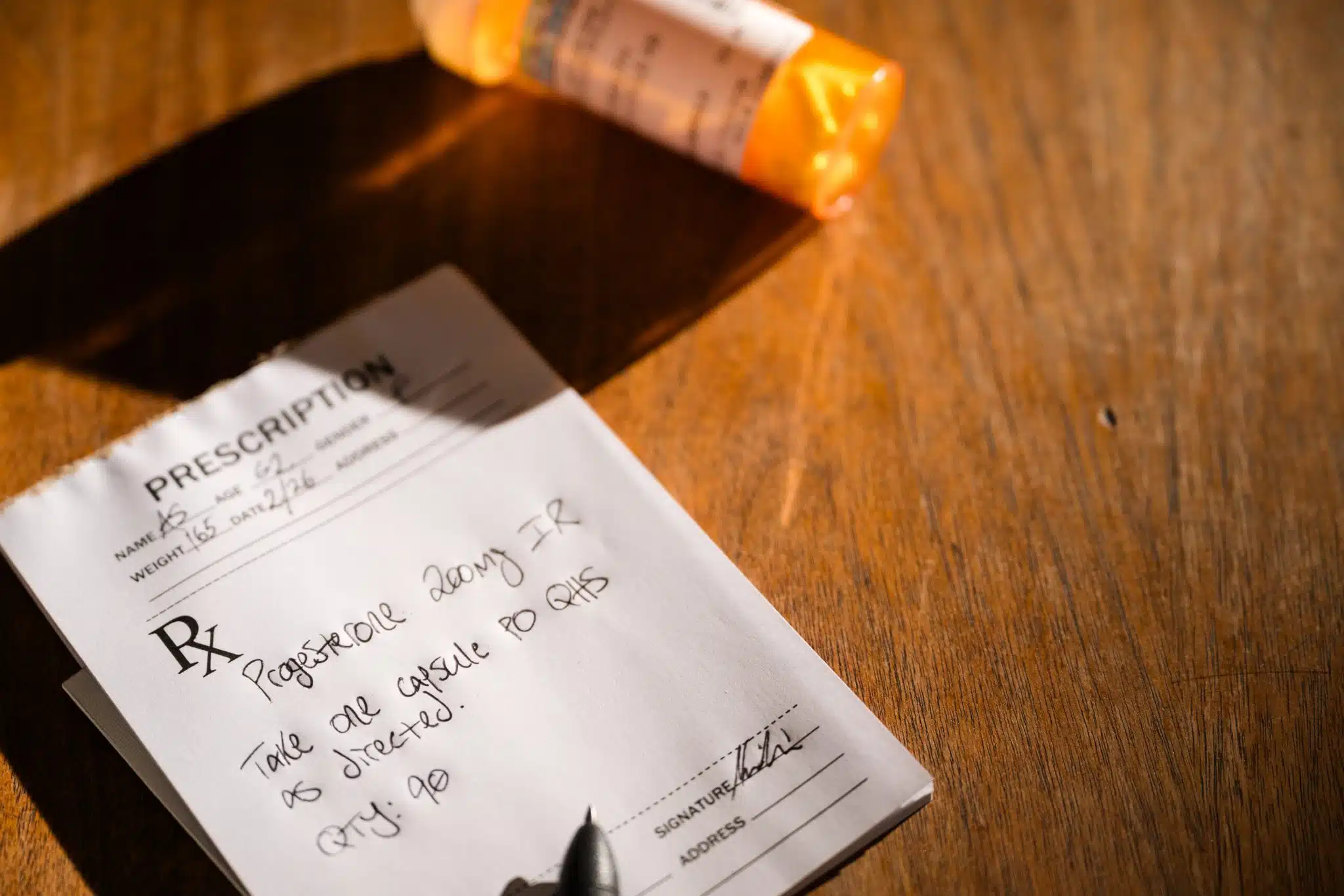 HRT Blog 16 Handwritten prescription for progesterone 200mg taken orally at bedtime, with an orange prescription bottle on a wooden surface